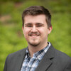 Headshot of Caden wearing a gray sport coat and a checkered shirt